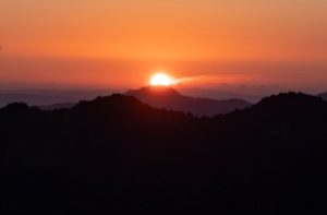 photo of an almost set sun behind a mountain range