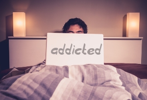 photo of a man in bed behind a laptop with the word addicted on it
